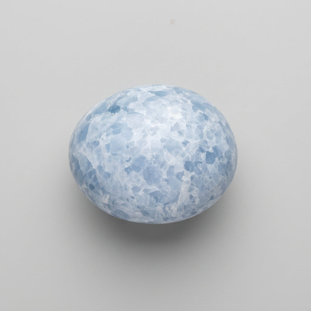 A small oval blue-and-white marbled palm stone on a plain light background. Available from J.W.H. Designs Canada.