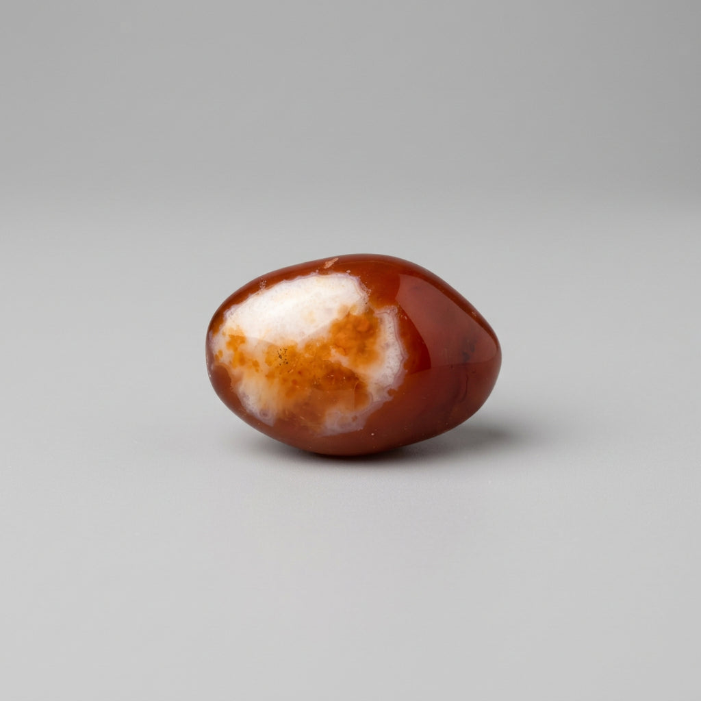 A polished brown and white agate stone displayed on a clear acrylic ring stand, positioned above a clear plastic ruler for scale on a plain off-white background. J.W.H Designs