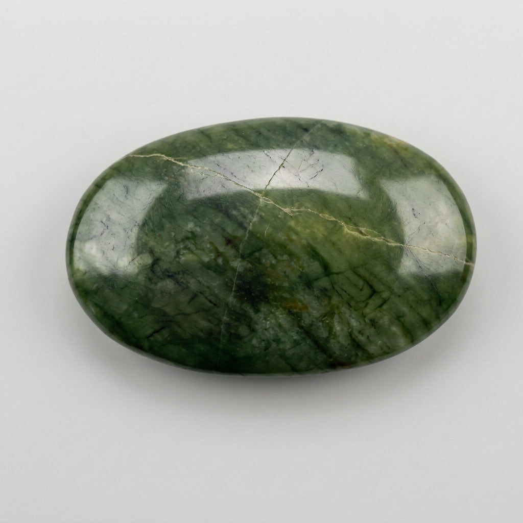 A polished oval green stone with natural marbled veining, resting on a plain white surface by J.W.H. Designs.
